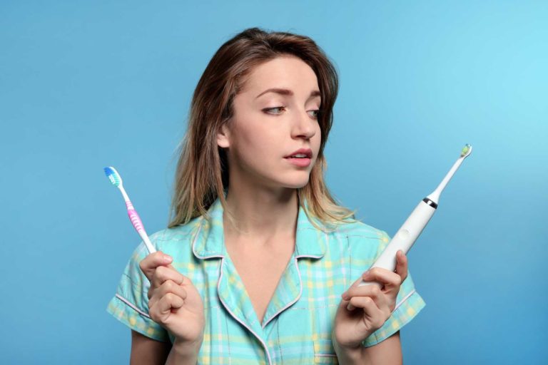 Woman holding an electric toothbrush and a manual toothbrush.